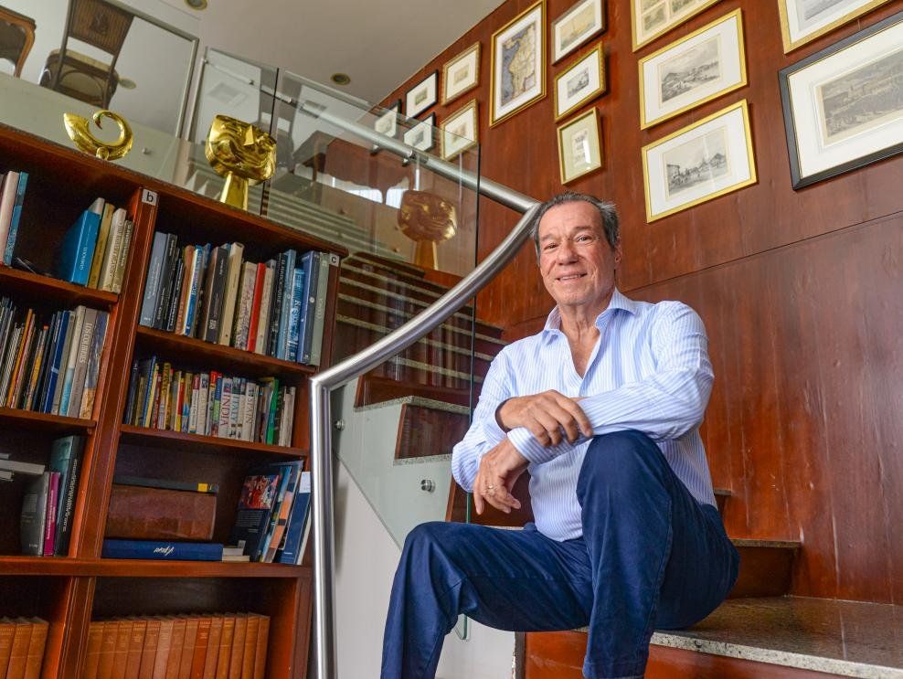 Benjamín Rosales Valenzuela sentado en la escalera de su biblioteca, rodeado de libros y grabados antiguos