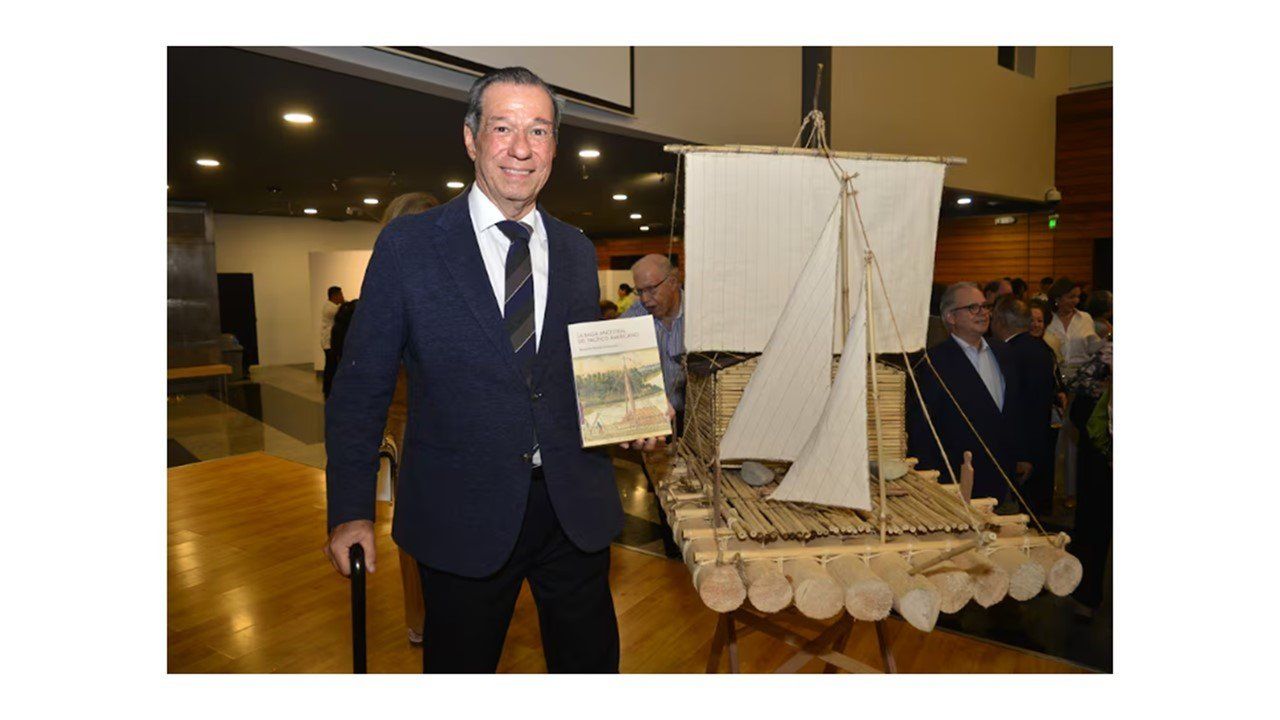Benjamín Rosales sostiene su libro junto a una maqueta de balsa con velas en el MAAC