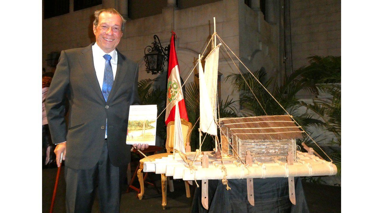 Benjamín Rosales con su libro junto a una maqueta de balsa y la bandera del Perú en Lima