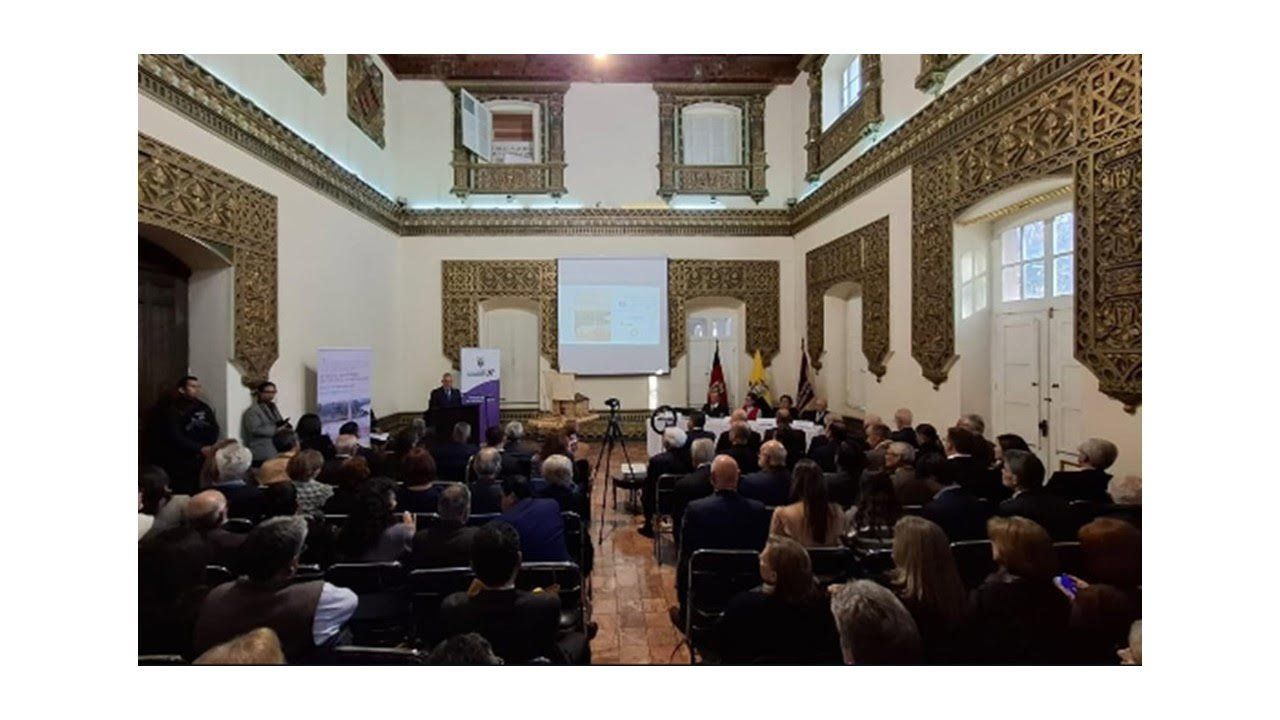 Salón colonial con decoración dorada lleno de público durante la presentación en Quito